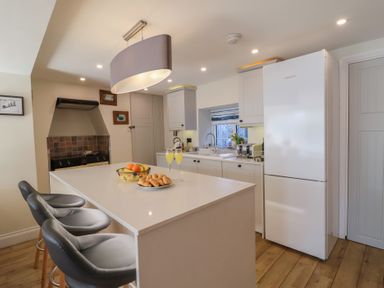 A kitchen with an island counter with fruit bowl and croissants and three grey stools at Rosebank Cottage in Mortehoe