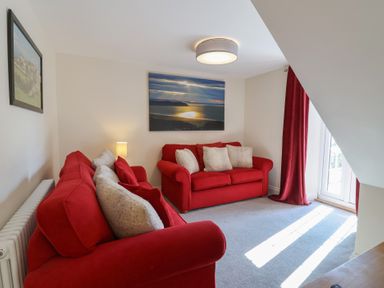 A living room with two red sofas and cushions a lamp and wall art at Rosebank Cottage in Mortehoe
