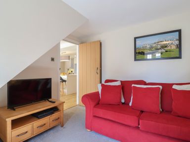 A living room with a red sofa and television on a wooden stand at Rosebank Cottage in Mortehoe