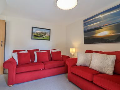 A room with two red sofas with cushions a small lamp and landscape pictures on the walls at Rosebank Cottage in Mortehoe