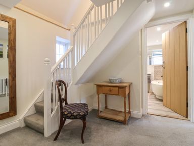 A staircase with a wooden chair and a small wooden table with a bowl next to a bathroom door at Rosebank Cottage in Mortehoe