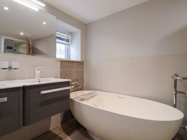A bathroom with a white freestanding bathtub a dark vanity with two sinks a large mirror and a window at Rosebank Cottage in Mortehoe