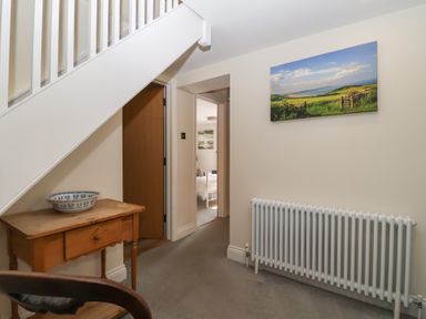 A hallway with a wooden table and a bowl under stairs a radiator and a landscape picture on the wall at Rosebank Cottage in Mortehoe