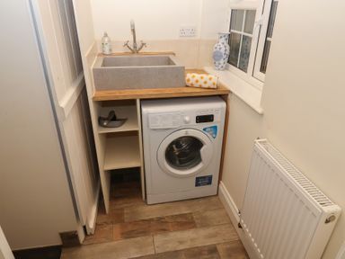 A laundry room with a washing machine under a sink a vase on the windowsill and a radiator on the wall at Rosebank Cottage in Mortehoe