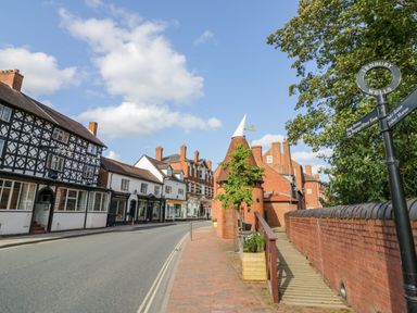 A street with timber framed and brick buildings with a brick walkway and directional signpost in Tenbury Wells