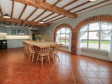 A kitchen and dining area with a wooden dining table and chairs under wooden ceiling beams and arched windows at Hunters Moon in Tenbury Wells