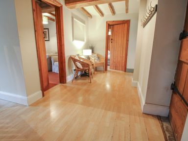 A hallway with wooden floor and two wicker chairs with cushions a lamp a door with wooden beams and hooks on the wall at Hunters Moon in Tenbury Wells