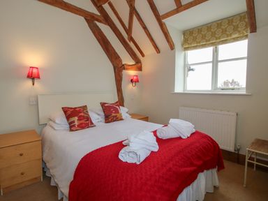 A bedroom with a double bed red throw and white towels on it with wooden beams on the ceiling at Hunters Moon in Tenbury Wells