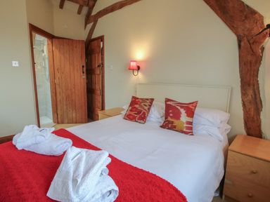 A bedroom with a double bed with red pillows and a red blanket with folded white towels and wooden furniture at Hunters Moon in Tenbury Wells