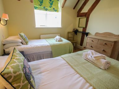 A bedroom with two single beds green bed covers wooden dresser and window with patterned blind at Hunters Moon in Tenbury Wells
