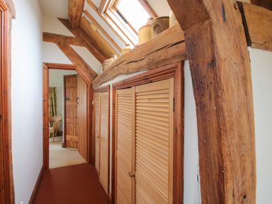 A narrow corridor with wooden beams overhead lockers on the right and a wooden door at the end at Hunters Moon in Tenbury Wells