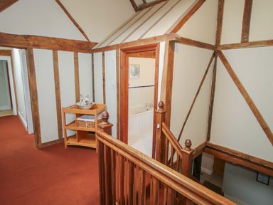 A hallway with wooden beams and a small shelving unit next to a stair railing and bathroom at Hunters Moon in Tenbury Wells