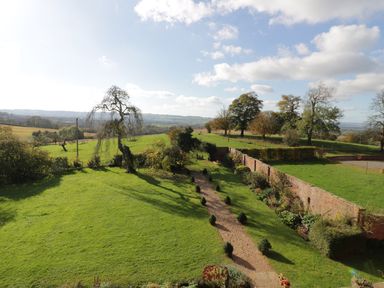 A garden with a gravel pathway lined with small shrubs and adjacent brick wall with flowers beyond a lawn at Hilltop House in Tenbury Wells