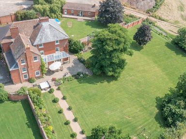 An aerial view of a large brick house with a patio and umbrella in the garden at Hilltop House in Tenbury Wells