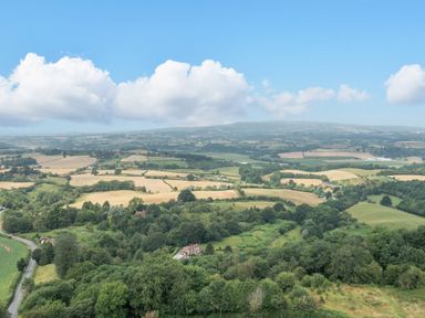 A landscape view of farmland fields and trees with a road and houses in the distance at Hilltop House in Tenbury Wells