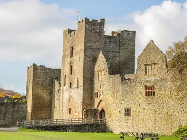 An old stone castle with towers and a flag on a grassy area with picnic tables at Hilltop House in Tenbury Wells