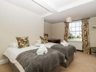 A bedroom with two single beds with pillows and rolled towels by a window with floral curtains at Hilltop House in Tenbury Wells