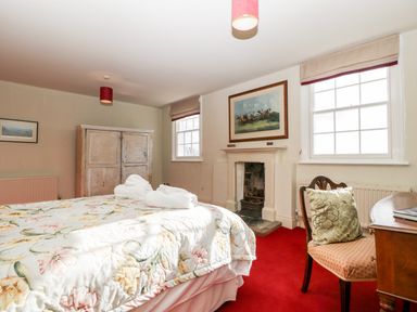 A bedroom with a floral bedspread two rolled towels a wooden wardrobe a small fireplace and a desk with a chair and cushion at Hilltop House in Tenbury Wells