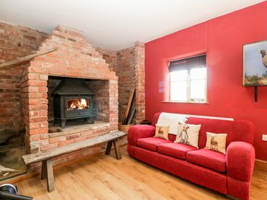 A room with a brick fireplace and a wood burning stove a red sofa with cushions under a window with a blind at Hilltop House in Tenbury Wells