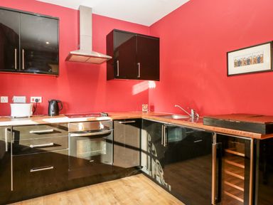 A kitchen with black cabinets red walls wooden countertop oven stovetop toaster kettle and a sink at Hilltop House in Tenbury Wells