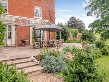 An outdoor patio with a dining table and chairs under an umbrella next to a brick building and garden at Hilltop House in Tenbury Wells