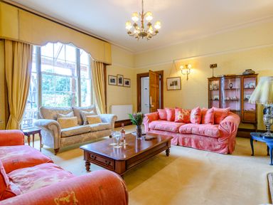 A living room with sofas a wooden coffee table a display cabinet and large windows at Hilltop House in Tenbury Wells