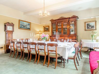 A dining room with a long table set with glassware and candlesticks surrounded by wooden chairs a large wooden cabinet and clock on the wall at Hilltop House in Tenbury Wells