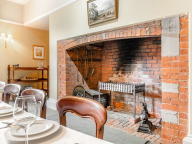 A dining room with a brick fireplace wooden chairs and a set table at Hilltop House in Tenbury Wells