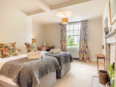 A bedroom with two single beds with grey throws and cactus patterned pillows and a window with floral curtains at Hilltop House in Tenbury Wells