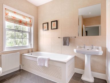 A bathroom with a bathtub a pedestal sink and a window with patterned blinds at Hilltop House in Tenbury Wells