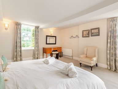 A bedroom with a bed towels and cushions a wooden desk with a mirror an armchair and curtains at Hilltop House in Tenbury Wells