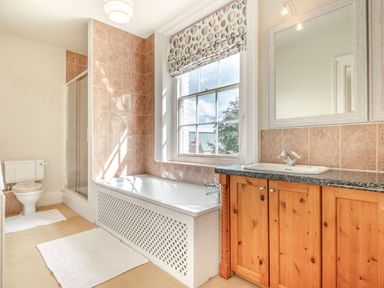 A bathroom with a bathtub under a window a wooden vanity with a sink a toilet and a shower at Hilltop House in Tenbury Wells