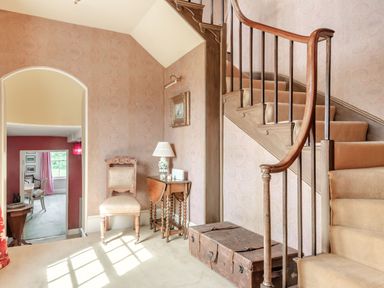 A hallway with a carpeted staircase a wooden chair a small table with a lamp and a vintage trunk near an archway leading to another room at Hilltop House in Tenbury Wells