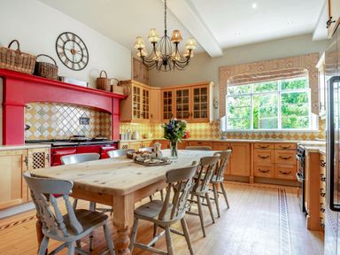 A kitchen with a wooden dining table and chairs under a chandelier at Hilltop House in Tenbury Wells