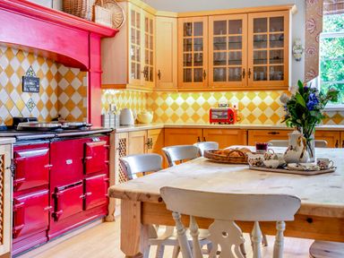 A kitchen with a red stove wooden cabinets a wooden table with chairs and a flower vase at Hilltop House in Tenbury Wells