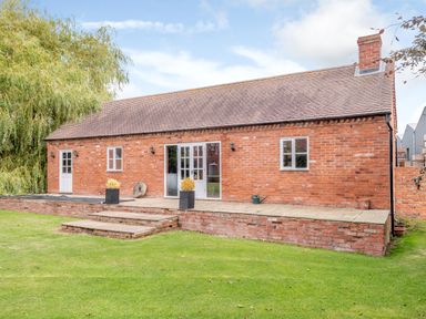 A brick house with a tiled roof and a raised paved patio with steps leading to a lawn at Hilltop House in Tenbury Wells