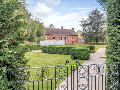 A garden with trimmed hedges and an above ground pool in front of a brick house at Hilltop House in Tenbury Wells