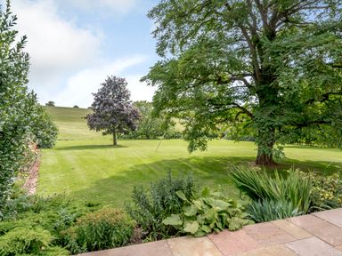 A garden with grass lawn trees shrubs and a stone patio at Hilltop House in Tenbury Wells