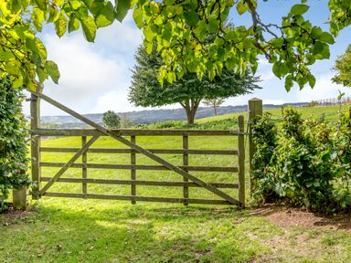 A wooden gate opening to a green field with trees and bushes at Hilltop House in Tenbury Wells
