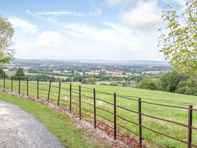 A rural landscape with green fields trees a metal fence and a gravel path at Hilltop House in Tenbury Wells
