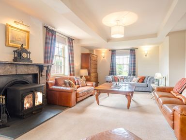 A living room with leather sofas a wood burning stove and a wooden coffee table at Hilltop House in Tenbury Wells