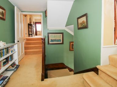 A stairway with green walls and beige carpet with paintings hanging on the walls and a bookshelf on the left at Hilltop House in Tenbury Wells