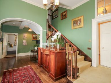 A hallway with green walls a wooden sideboard a staircase and a red rug at Hilltop House in Tenbury Wells