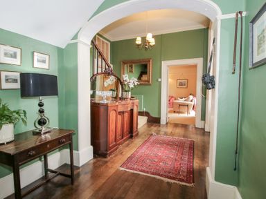 A hallway with green walls wooden floor a red rug wooden furniture and a view into a living room at Hilltop House in Tenbury Wells