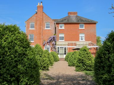 A brick house with white windows and a gravel pathway lined with bushes at Hilltop House in Tenbury Wells