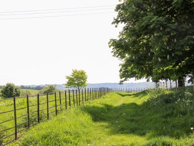 A fenced grassy path with trees and distant hills at Hilltop House in Tenbury Wells
