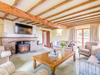 A living room with wooden beams a stone fireplace a flat screen tv sofas armchairs a wooden coffee table with flowers and wine glasses at The Chestnuts in Tenbury Wells