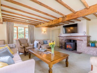 A living room with wooden beams a stone fireplace a wooden coffee table and sofas at The Chestnuts in Tenbury Wells