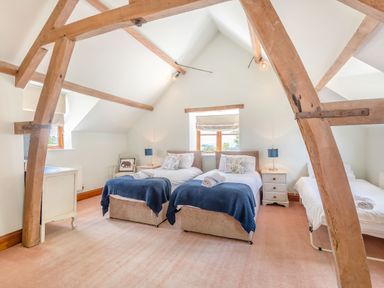 A bedroom with three beds wooden beams and two bedside tables with lamps at The Chestnuts in Tenbury Wells