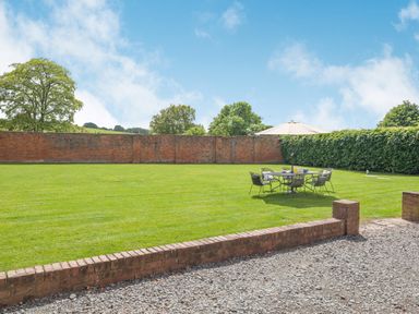 A garden with a lawn table set and umbrella surrounded by brick walls and hedges at The Chestnuts in Tenbury Wells